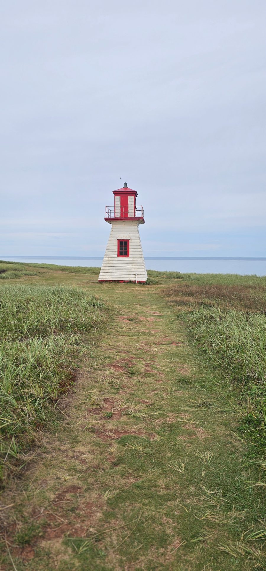 Sentier herbeux menant à un phare blanc et rouge au bord de la mer